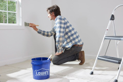 lifestyle photography of man painting walls with a Lowe's bucket in front of him for United Solutions in Leominster, MA