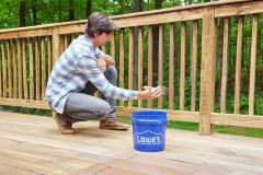 lifestyle photography of man staining porch railings using a lowe's bucket for United Solutions in Leominster, MA