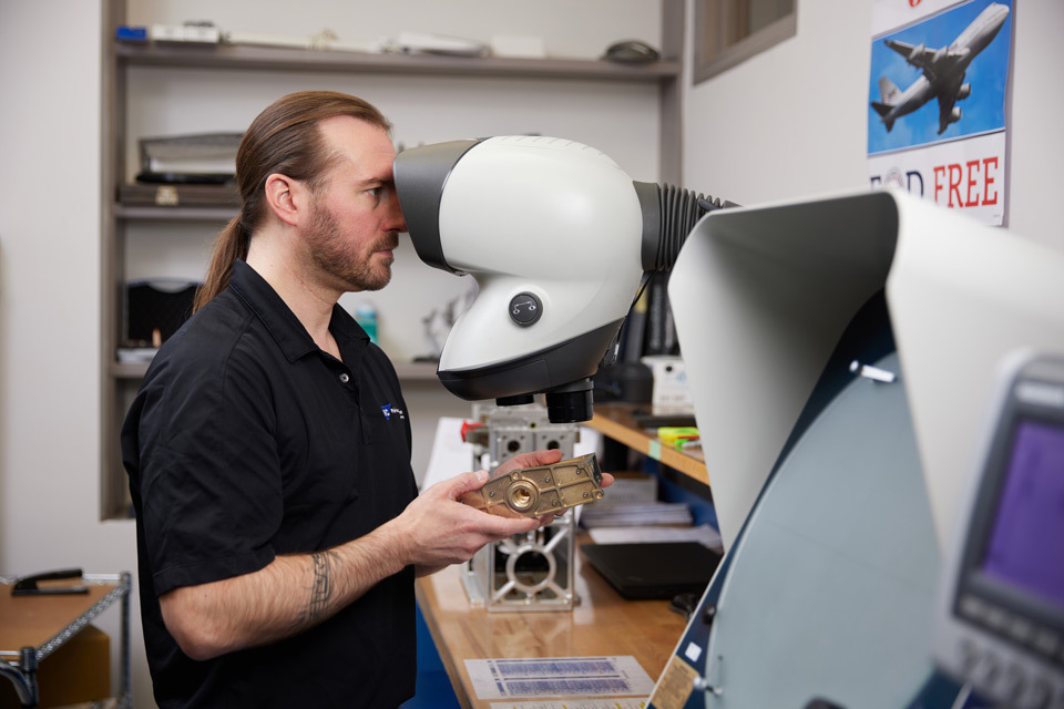 Fairview onsite lifestyle photography for Fairview Fitting in Woburn, MA onsite lifestyle photography of male employee looking through machine to inspect product for Fairview Fitting of Woburn, MA