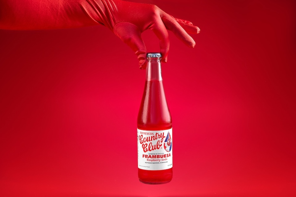 Food photography of a bottled soft drink against a red background  being held by a red-gloved hand for La Esquina of Lynn, MA