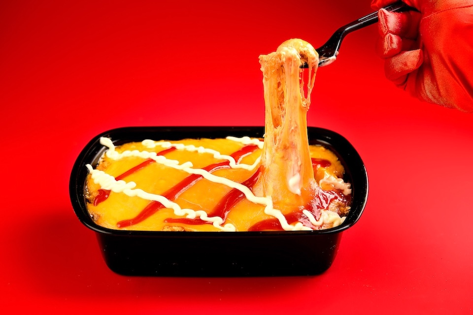 Food photography of a cheese casserole dish on a red background with a red gloved hand doing a cheese pull with a fork for La Esquina of Lynn, MA
