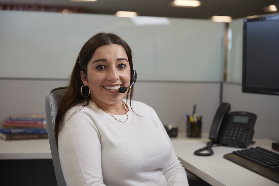 Lifestyle photography of female employee seated in a cubicle with a headset on, smiling. For Hitachi High Tech America of Westford, MA.