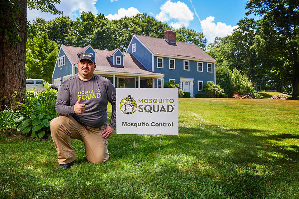lifestyle photography of mosquito squad employee kneeling next to the company sign giving a thumbs up in a lawn for Mosquito Squad of Chelmsford, MA.