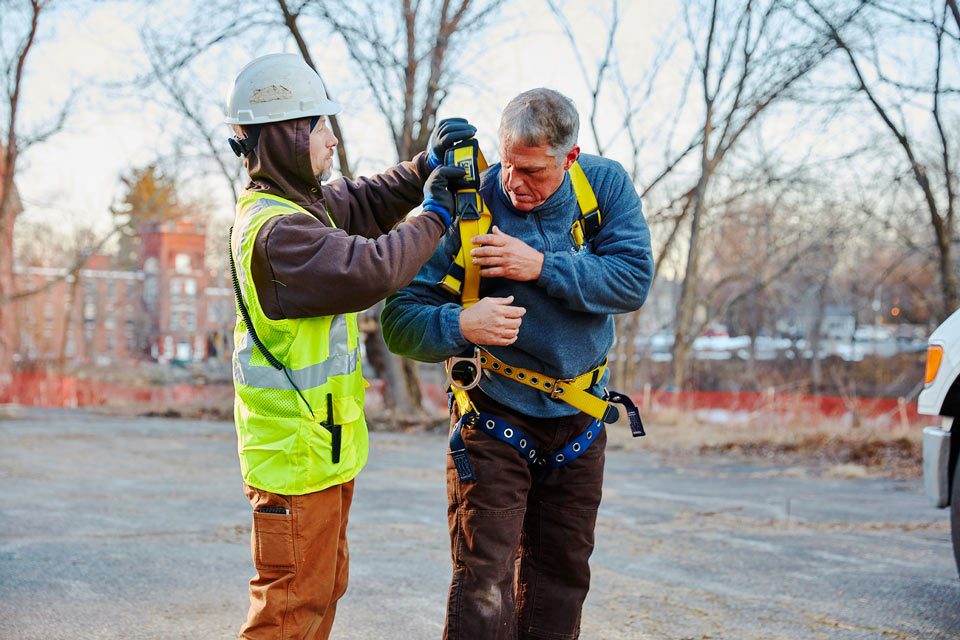 lifestyle photography of contruction worker helping coworker put on a harness and safety straps
