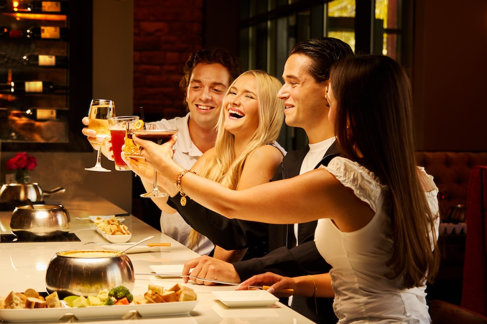 lifestyle photography of a group of 4 young adults smiling and raising their drinks at Melting Pot of Bedford, MA