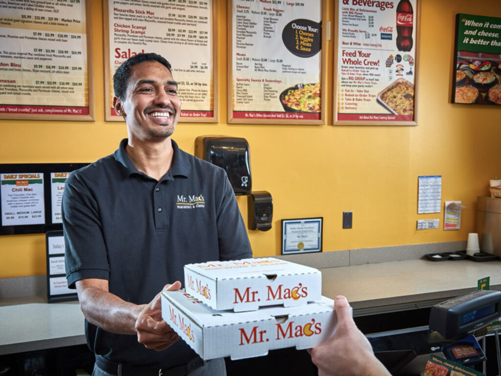 Lifestyle photography of Mr. Mac's male employee handing box of food to a customer.