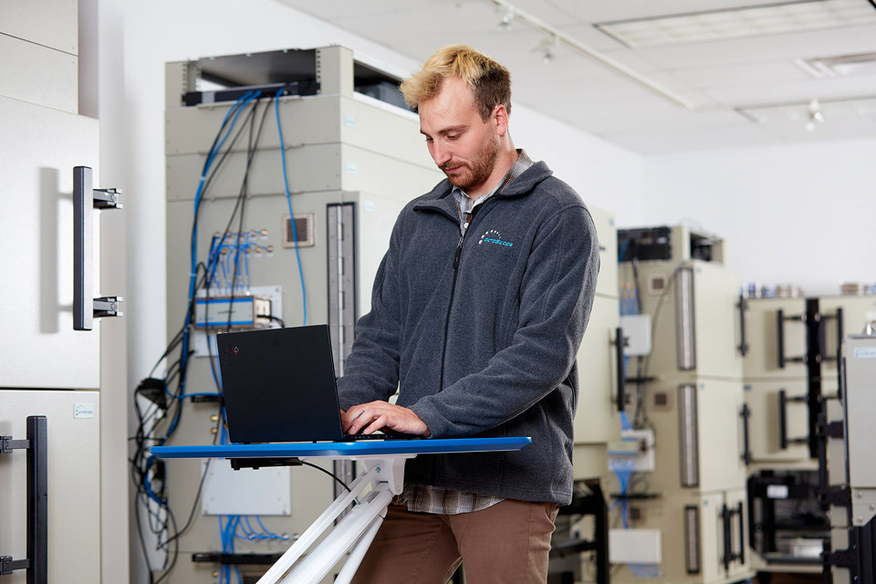 lifestyle photography of male employee standing, typing on a laptop for Octoscope of Littleton, MA.