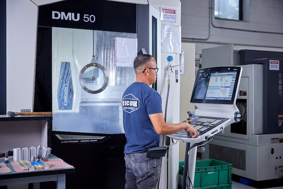 Onsite lifestyle photography of worker standing at control panel of 5 axis milling machine for Precision Technologies of Tyngborough, MA.