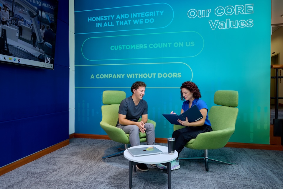 Lifestyle Photography of male employee seated across female employee with binder discussing at Teradyne of North Reading, MA.