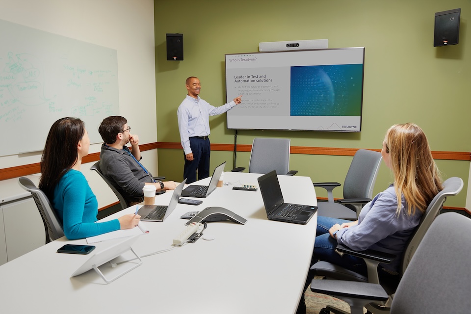 Lifestyle photography of employee presenting to a group of three employees in a conference room at Teradyne of North Reading, MA.