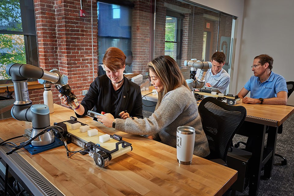 Onsite lifestyle photography of 4 people sat at desks in pairs testing robots for Universal Robots of Boston, MA.
